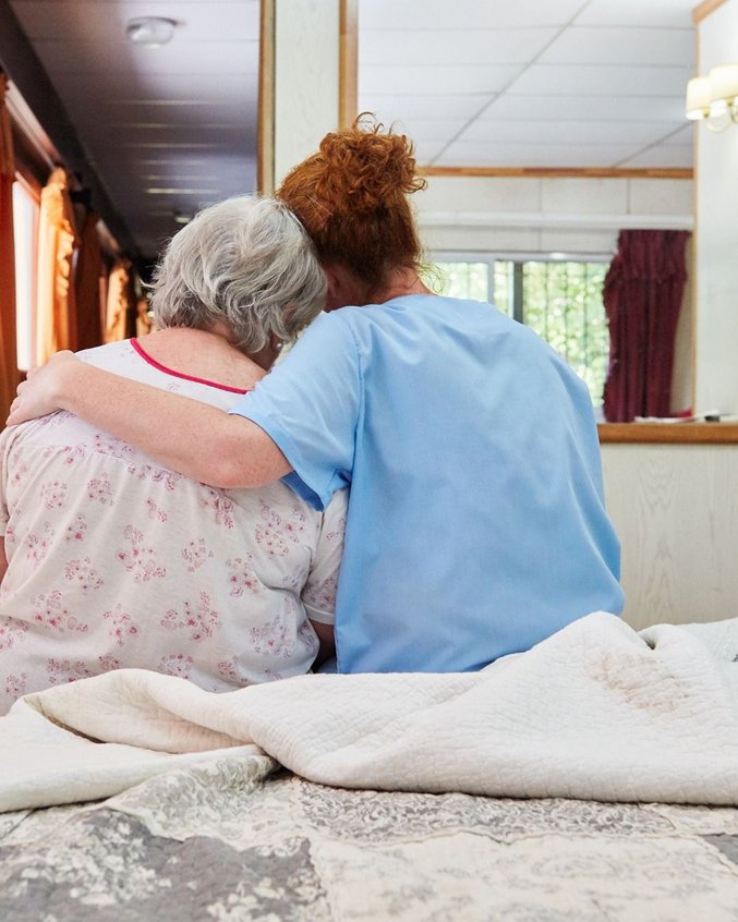 Carer comforting an older woman sitting on her bed