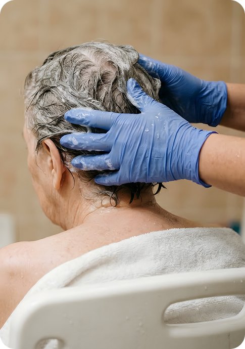 Carer wearing gloves washing an older woman’s hair