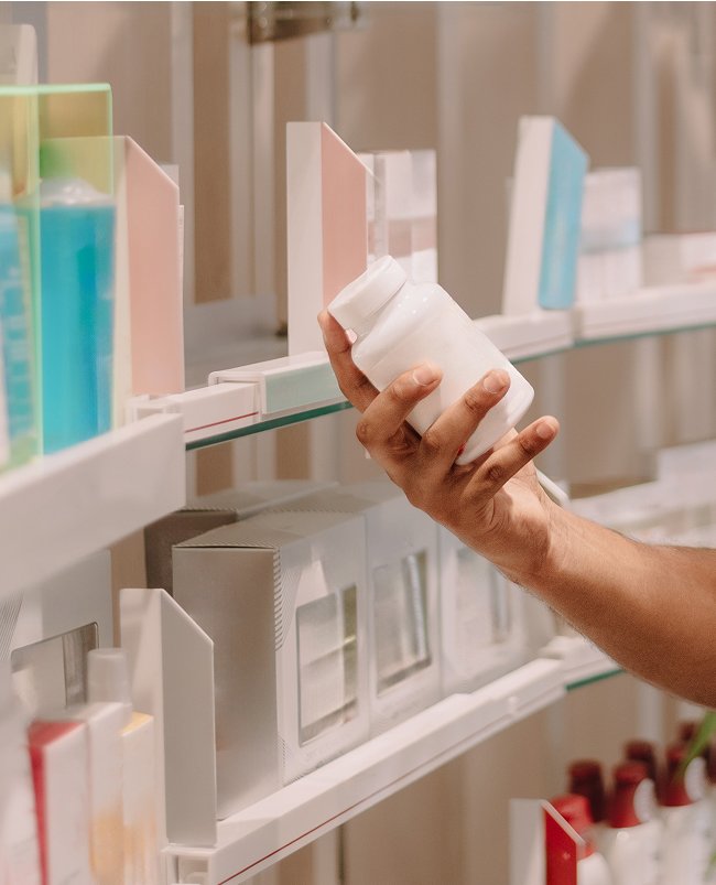 Hand reaching for a medicine bottle on a pharmacy shelf