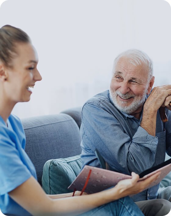 Carer chatting with a smiling older man on the couch at home