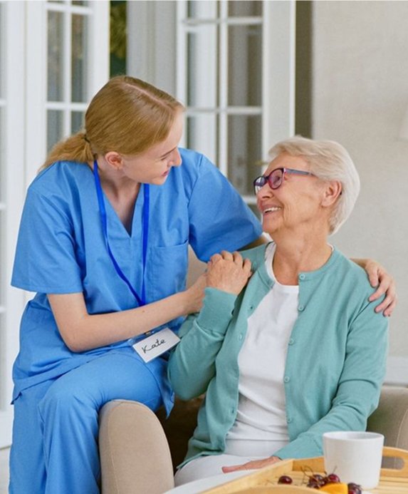Carer in blue scrubs sitting and chatting with an older woman