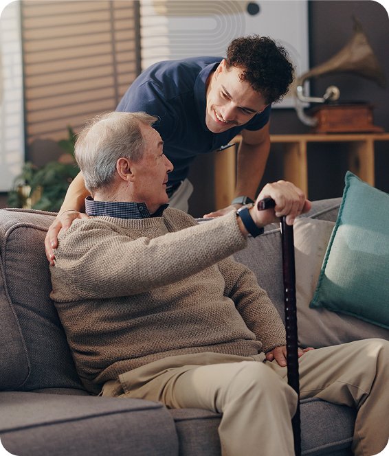 Support worker helping an older man with a walking stick stand up from the couch