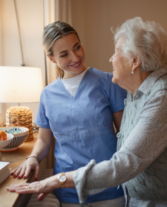 Carer in blue scrubs talking with an older woman at home