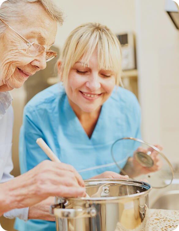 Smiling carer in blue scrubs writing notes beside an older woman