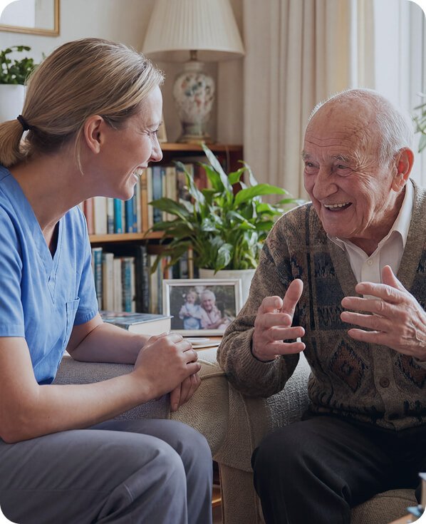 Carer in blue scrubs chatting with a smiling older man at home