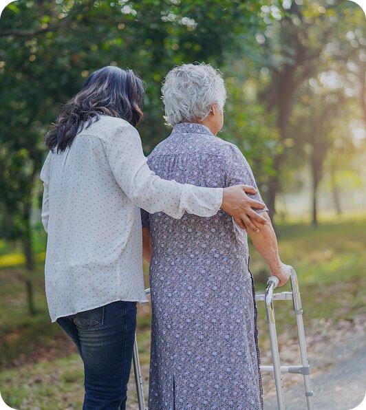 Carer walking arm in arm with an older woman using a walking frame outdoors