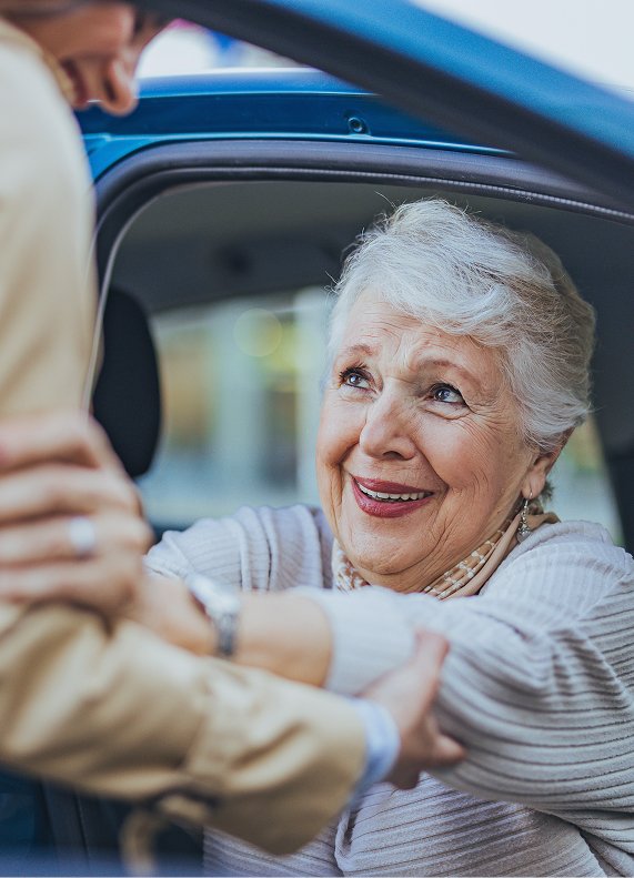 Smiling older woman getting into a car with help from a support worker