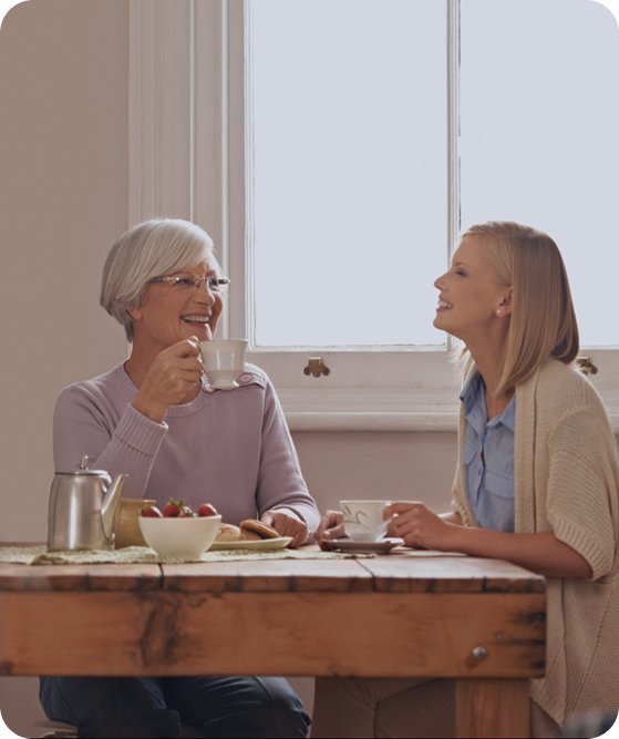 Two women chatting and laughing over tea at a kitchen table